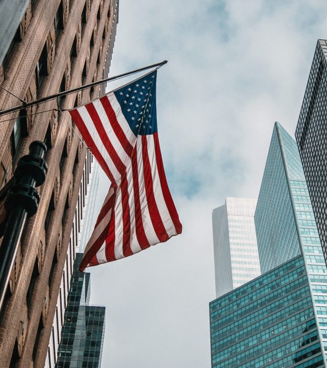 the usa or united states of america flag on a flagpole near skyscrapers under a cloudy sky